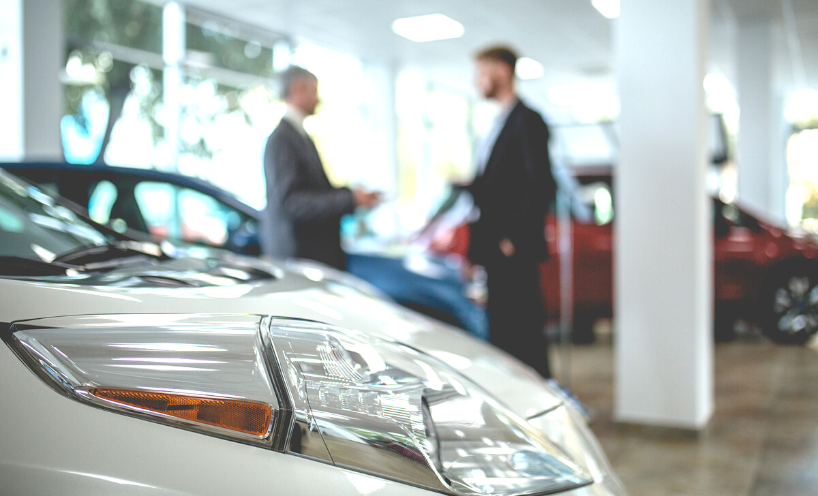 two men are talking at a car dealership